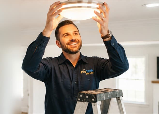Smiling electrician on a stepladder fitting a ceiling light in a home