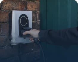 Hand plugging a cable into a wall-mounted EV charger