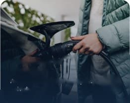 Person holding an EV charging connector next to a car